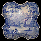 Pearlware saucer printed underglaze in blue. Design based on print entitled “Nuneham Courtenay, Bridge and Cottage”  by S. Owen and published in 1811. Continuous repeating floral border of wild roses. This pattern was used by most major and many minor potteries in the second quarter of the nineteenth century (Coysh and Henrywood 1982, 1989). This design, although based on a print of an actual location, is a better fit in the Pastoral category, for its rural location and fishing theme.